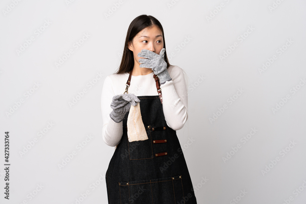 Chinese fishmonger wearing an apron and holding a raw fish over isolated white background doing surprise gesture while looking to the side Chinese fishmonger wearing an apron and holding a raw fish over isolated white background doing surprise gesture while looking to the side