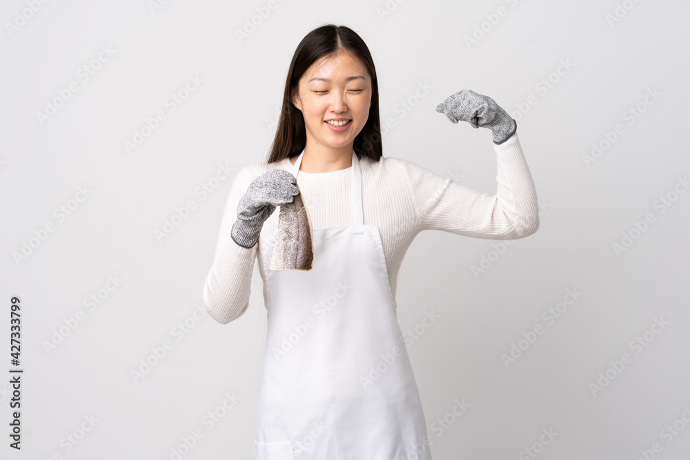 Chinese fishmonger wearing an apron and holding a raw fish over isolated white background doing strong gesture Chinese fishmonger wearing an apron and holding a raw fish over isolated white background doing strong gesture