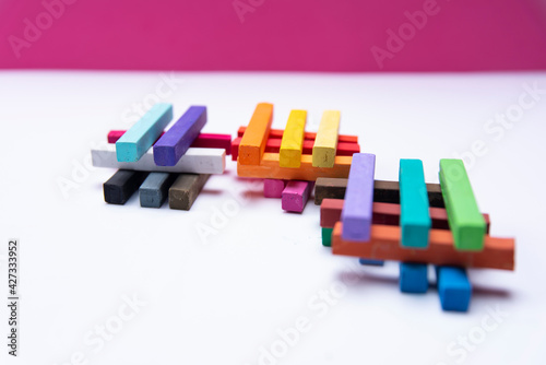 GROUPS OF COLORED CHALKS IN PILES ON A WHITE AND PINK BACKGROUND