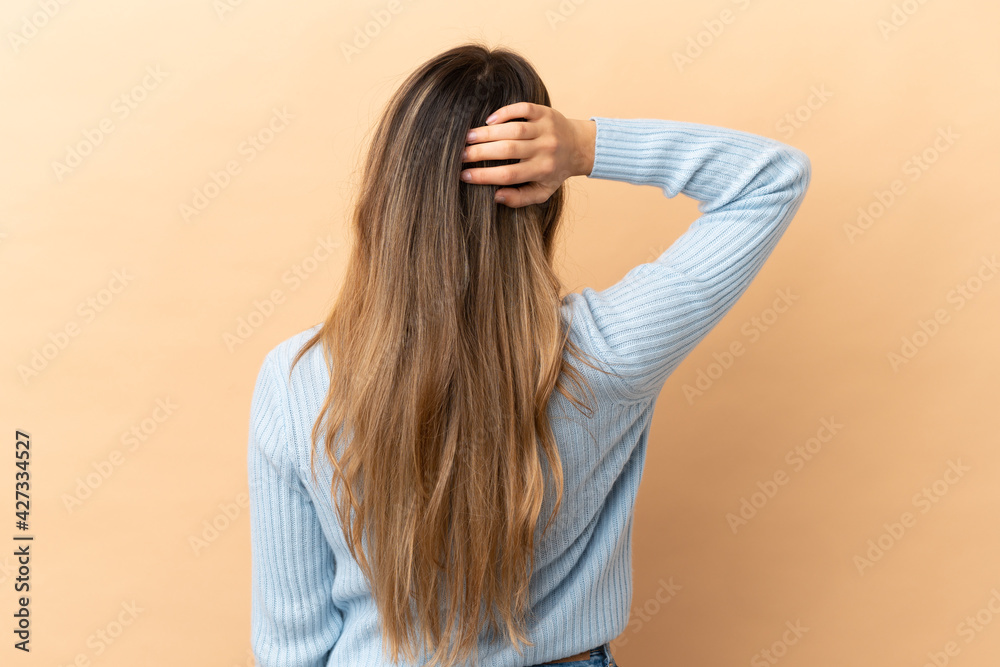 Fototapeta premium Young caucasian woman isolated on beige background in back position and thinking