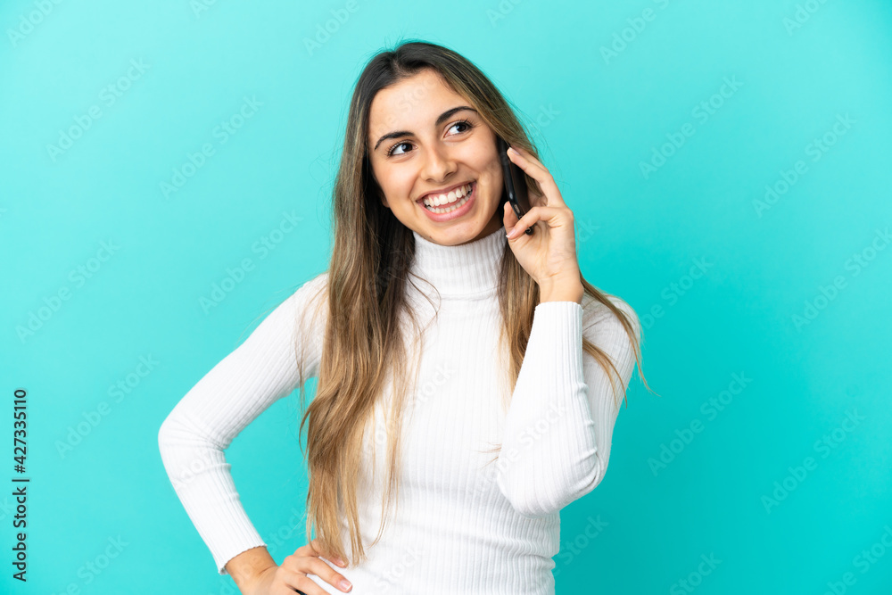 Young caucasian woman using mobile phone isolated on blue background posing with arms at hip and smiling Young caucasian woman using mobile phone isolated on blue background posing with arms at hip and smiling