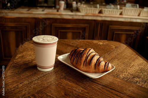 Croissant with coffee to go in a paper cup, take away breakfast