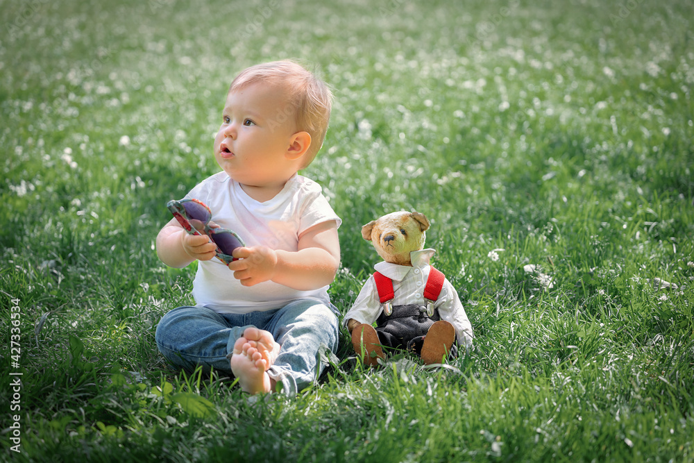 little boy 1 year old sitting on green grass in park with teddy bear toy, happy childhood little boy 1 year old sitting on green grass in park with teddy bear toy, happy childhood