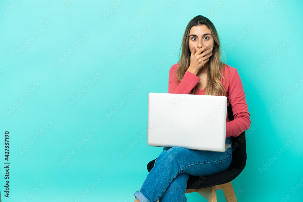 Young caucasian woman sitting on a chair with her pc isolated on blue background surprised and shocked while looking right Young caucasian woman sitting on a chair with her pc isolated on blue background surprised and shocked while looking right