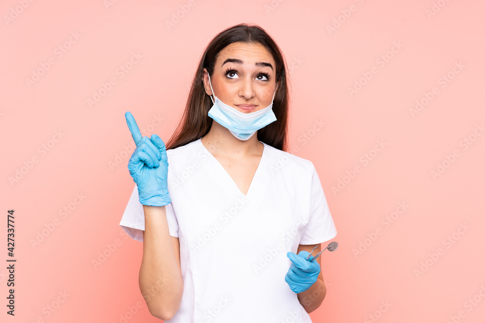 Woman dentist holding tools isolated on pink background pointing with the index finger a great idea