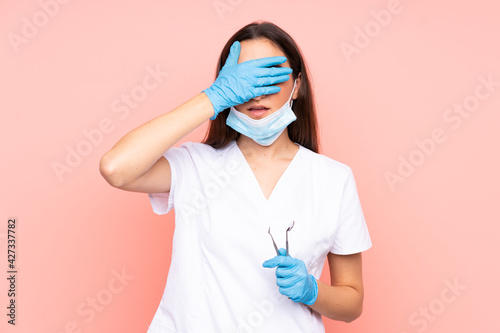 Woman dentist holding tools isolated on pink background covering eyes by hands