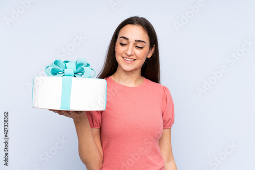 Pastry chef holding a big cake isolated on blue background with happy expression © luismolinero