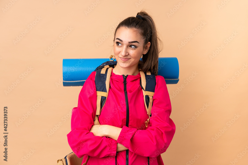 Young mountaineer girl with a big backpacker isolated on beige background standing and looking to the side Young mountaineer girl with a big backpacker isolated on beige background standing and looking to the side