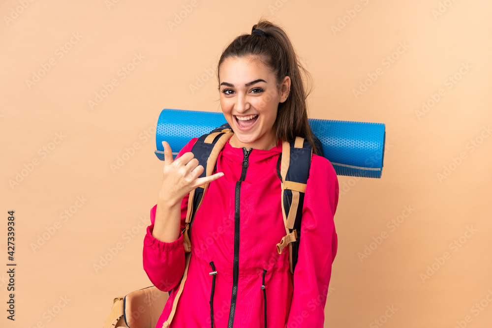 Young mountaineer girl with a big backpacker isolated on beige background making phone gesture Young mountaineer girl with a big backpacker isolated on beige background making phone gesture