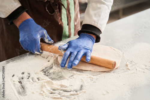 Baker man kneading dough on table with flour and rolling pin