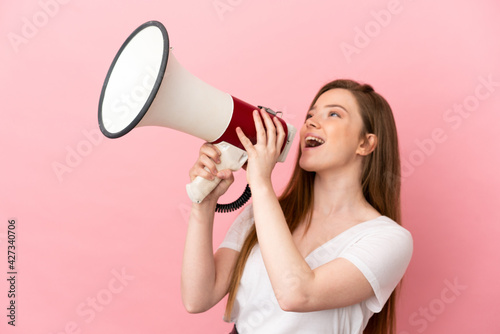 Teenager girl over isolated pink background shouting through a megaphone to announce something in lateral position