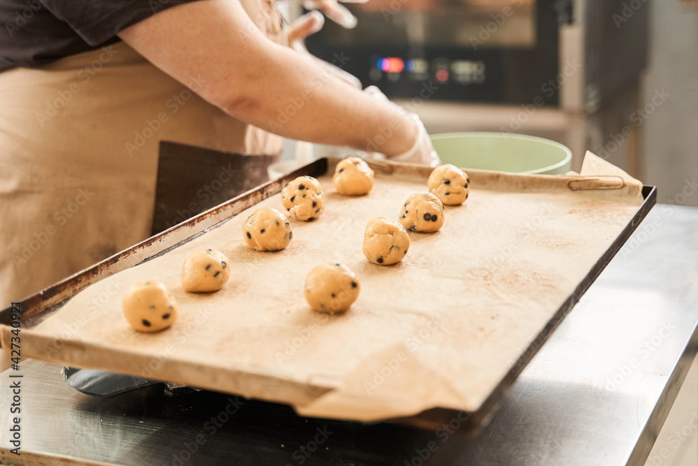 Baker putting ready-made dough balls at the tray with parchment paper