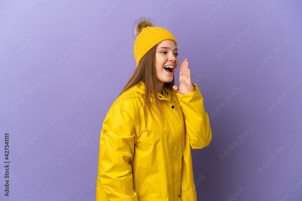 Teenager girl wearing a rainproof coat over isolated purple background shouting with mouth wide open to the side Teenager girl wearing a rainproof coat over isolated purple background shouting with mouth wide open to the side