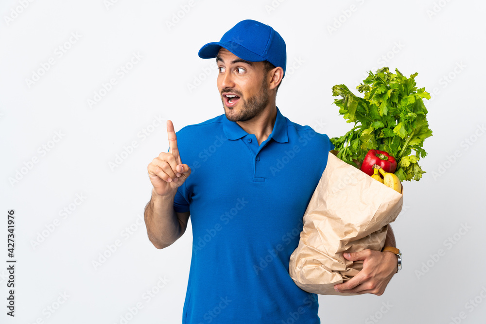 Delivery man with vegetables isolated on white background intending to realizes the solution while lifting a finger up Delivery man with vegetables isolated on white background intending to realizes the solution while lifting a finger up
