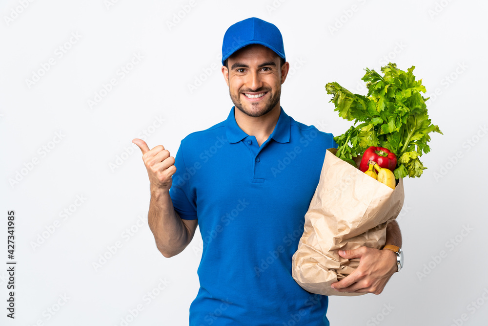 Delivery man with vegetables isolated on white background pointing to the side to present a product Delivery man with vegetables isolated on white background pointing to the side to present a product