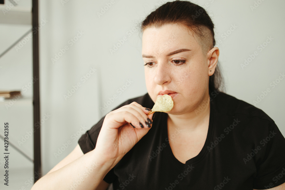 Overweight woman sitting on mat and eating chips Overweight woman sitting on mat and eating chips
