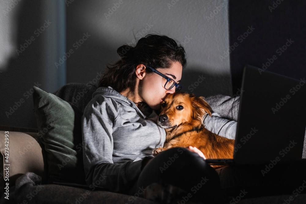 A young woman kisses her dog while watching a movie on her computer at  night. At home concept. Animal love. foto de Stock | Adobe Stock