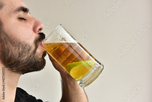 Bearded man drinking cold beer with lemon slice.