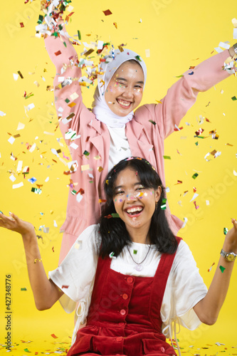 Closeup portrait of two young beautiful asian woman isolated on yellow background.