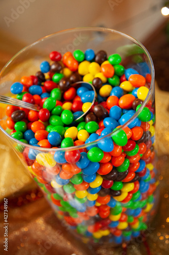 Glass jar full of m&m's with metal scoop. Colorful candy in clear glass jar