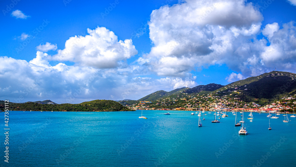 Sailboats float atop blue water in the bay of a tropical island during the day.