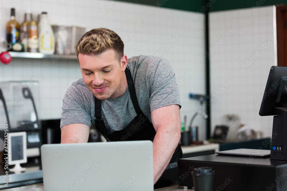 Barista cafe wearing apron and typing laptop computer at coffee shop with happy and smiling.. Worker making coffee on steam espresso coffee machine Barista cafe wearing apron and typing laptop computer at coffee shop with happy and smiling.. Worker making coffee on steam espresso coffee machine