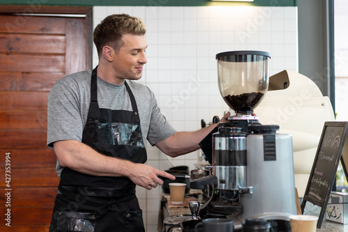 Barista cafe  wearing apron and prepare coffee grinder pour at coffee shop with happy and smiling. Worker making coffee on steam espresso coffee machine