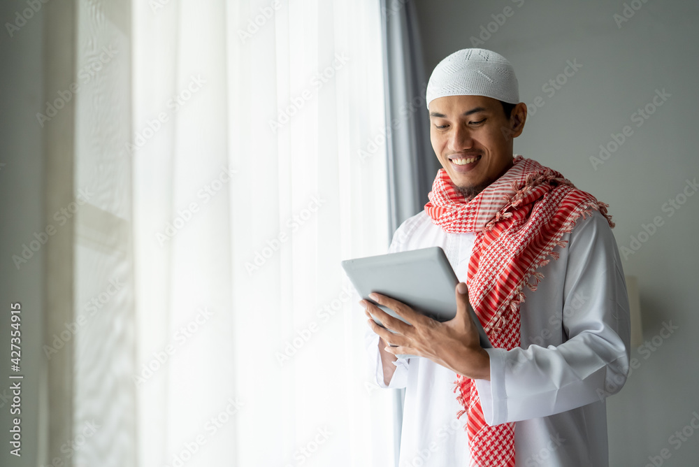 happy muslim businessman smiling while using tablet pc near window happy muslim businessman smiling while using tablet pc near window