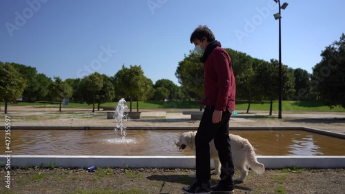 A Hispanic male in a mask walking and playing with his Golden Retriever in a park in slow motion - new normal concept photo