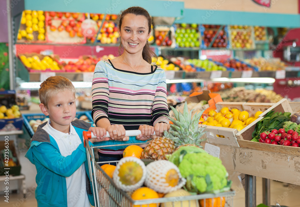 Little boy with his mother choosing fresh fruits and vegetables at supermarket
