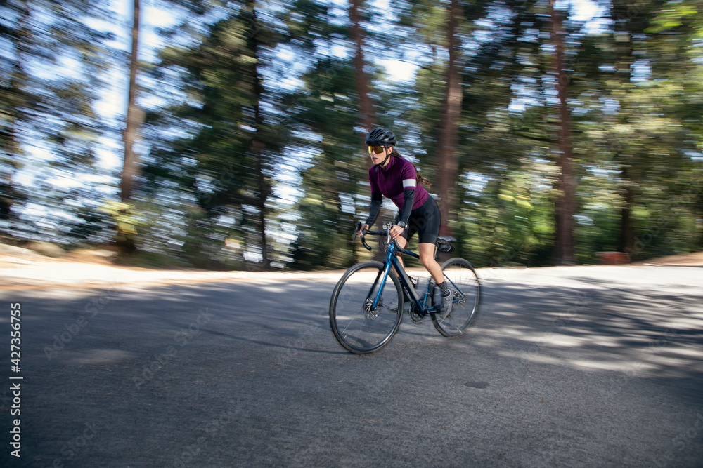 Fototapeta premium Mujer ciclista profesional a toda velocidad en una carretera en medio del bosque. Concepto de triatlón