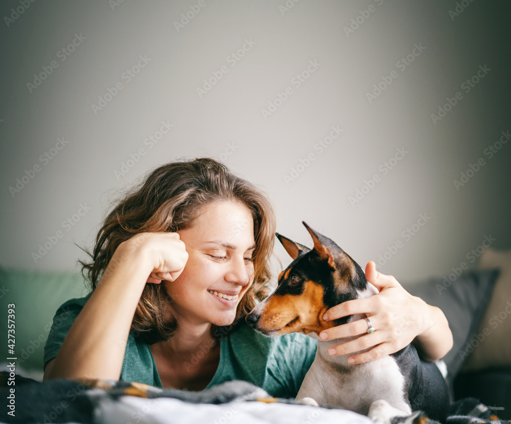 Obraz premium Beautiful happy young woman with african terrier bassenji dog on bed hugging tenderly, love pet