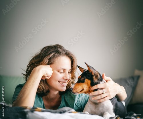 Beautiful happy young woman with african terrier bassenji dog on bed hugging tenderly, love pet