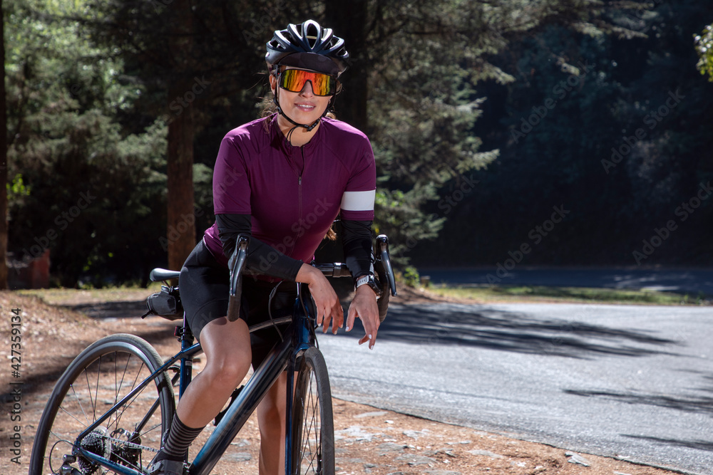 Mujer latina ciclista con su bicicleta de pista, usando casco y lentes de  sol, junto a la carretera en medio del bosque foto de Stock | Adobe Stock