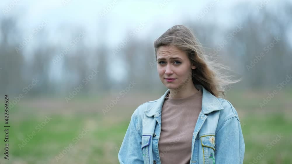 [4k] sceptical blonde woman looking at viewer standing outside on windy day