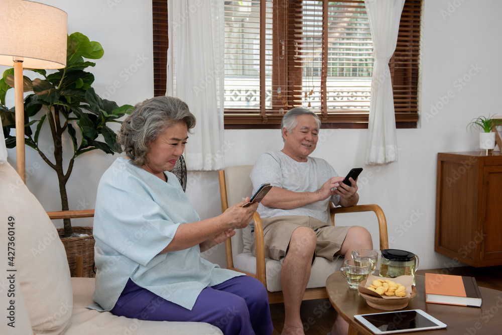 Fototapeta premium Happy Asian elderly family relaxing together at home. Senior couple using smartphone social media or online shopping. Retirement family husband and wife enjoy leisure activity with technology at home