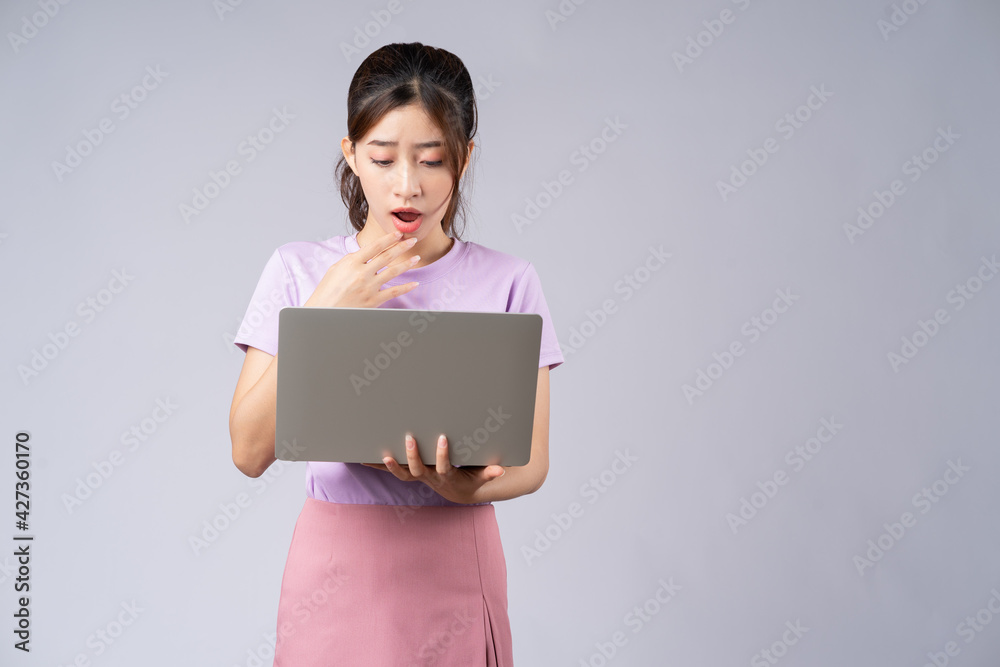 Young Asian woman using laptop on grey background Young Asian woman using laptop on grey background