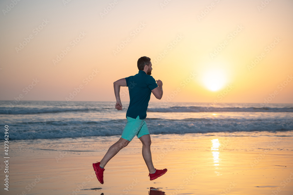 Athletic young man running on sea, colorful sunset sky.