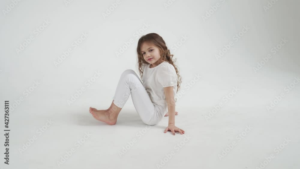 beautiful little girl with long hair in white clothes sits on the floor.