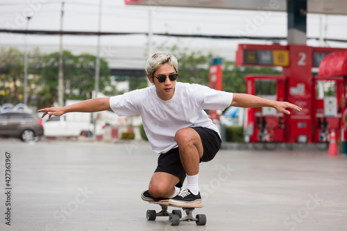 Asian young man skater riding on skateboard on courtyard at gas station with wear sunglasses. Young man skateboarding outdoor