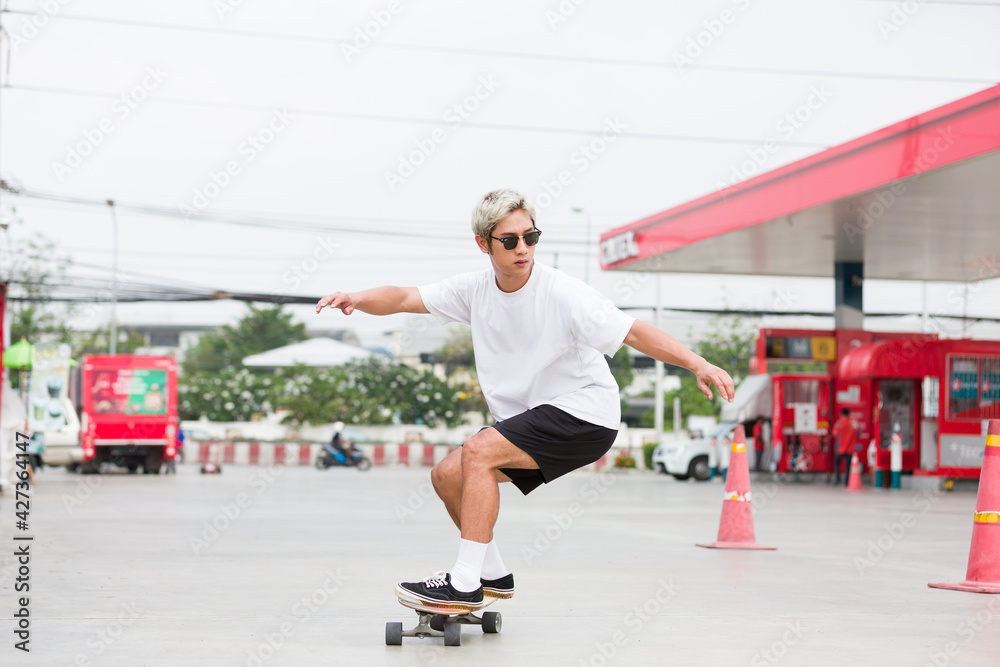 Asian young man skater riding on skateboard on courtyard at gas station with wear sunglasses. Young man skateboarding outdoor Asian young man skater riding on skateboard on courtyard at gas station with wear sunglasses. Young man skateboarding outdoor