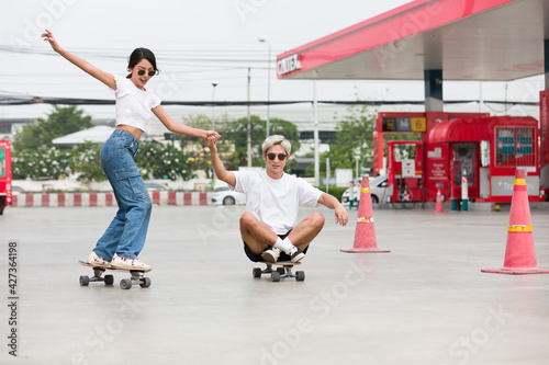 Asian young man and woman riding on skateboard on courtyard at gas station with wear sunglasses. Group of young teen people playing skateboarding outdoor