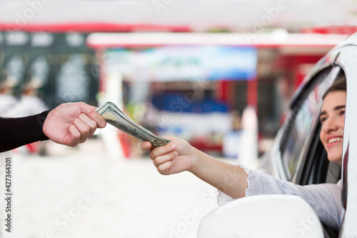 Attendant service worker receiving money from hand of customer at gas station. Customer giving money to hand worker at oil station. Refuelling car and paying by cash at gas pump