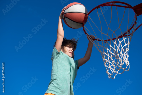 Kid little boy basketball player making slam dunk during basketball game.