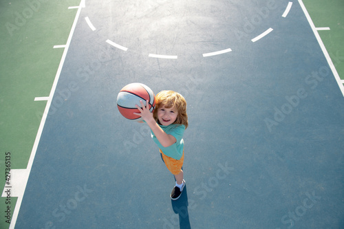 Child shooting Basketball ball and playing basketball, lower view wide angle. Kids sport activity. © Volodymyr