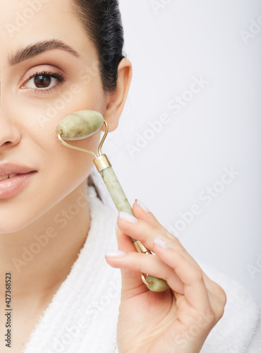 Face jade roller. Cropped half face of a Hispanic woman with jade or stone roller for anti-aging procedure