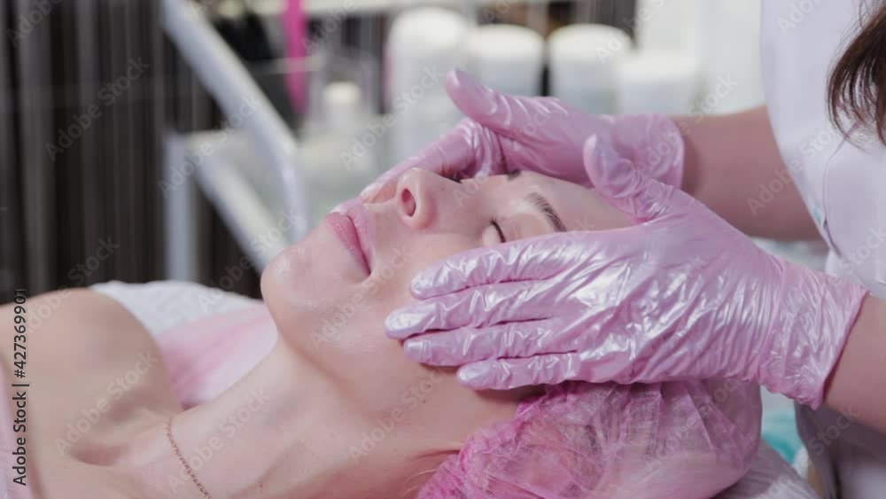 Woman beautician smears cream on the face of a female patient. Facial massage. Woman beautician smears cream on the face of a female patient. Facial massage.