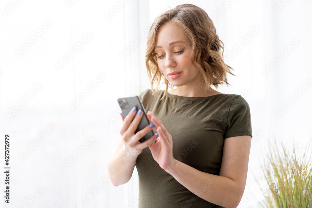 Pregnant woman use smartphone standing near big window Pregnant woman use smartphone standing near big window