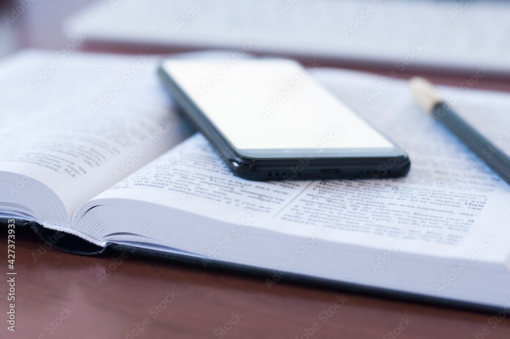 Open book Bible. Phone on the book. White blank screen. Empty table. Office workplace Open book Bible. Phone on the book. White blank screen. Empty table. Office workplace