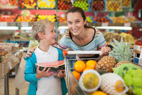 Portrait of happy woman and her little son with shopping cart full of fruits and vegetables